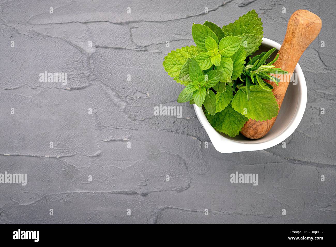 Alternative medicine fresh herbs in the stone mortar . Food ingredients and seasoning  peppermint , rosemarry and lemon balm  in a stone mortar set up Stock Photo
