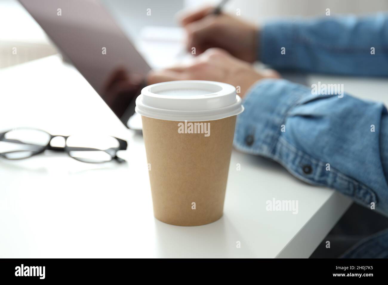 Blank paper cup against young man working on laptop. Stock Photo