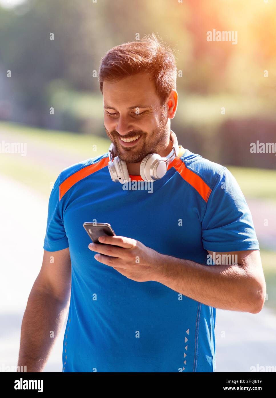 Smiling handsome man looking at mobile phone after recreation in park Stock Photo
