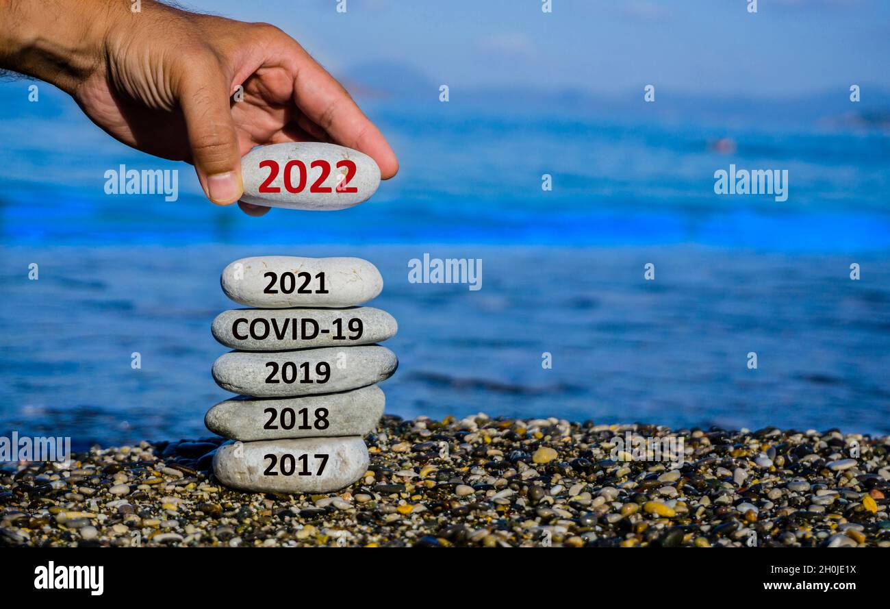 Happy new year 2022 is coming concept. Man adding stone to pebble tower because new year 2022 replace 2021. Beautiful conceptual photo. Stock Photo