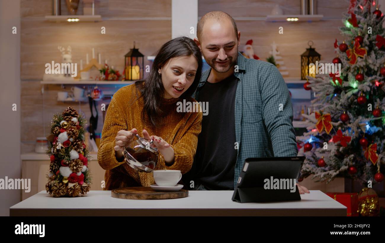 Couple using tablet for online video call on christmas eve. Man and woman chatting to family on conference via internet for holiday season celebration. Festive people in xmas decorated home Stock Photo