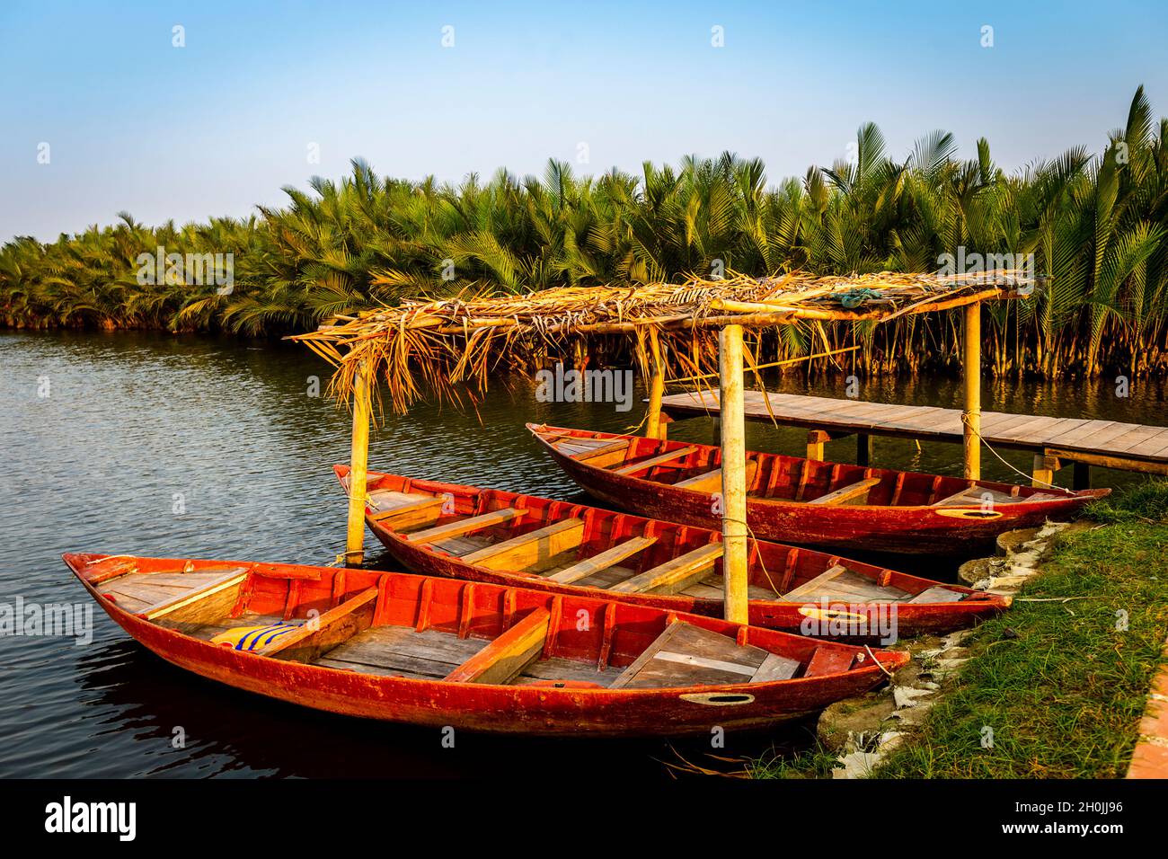 Three red boats all tied up together next to a dock with many palm trees behind. Stock Photo