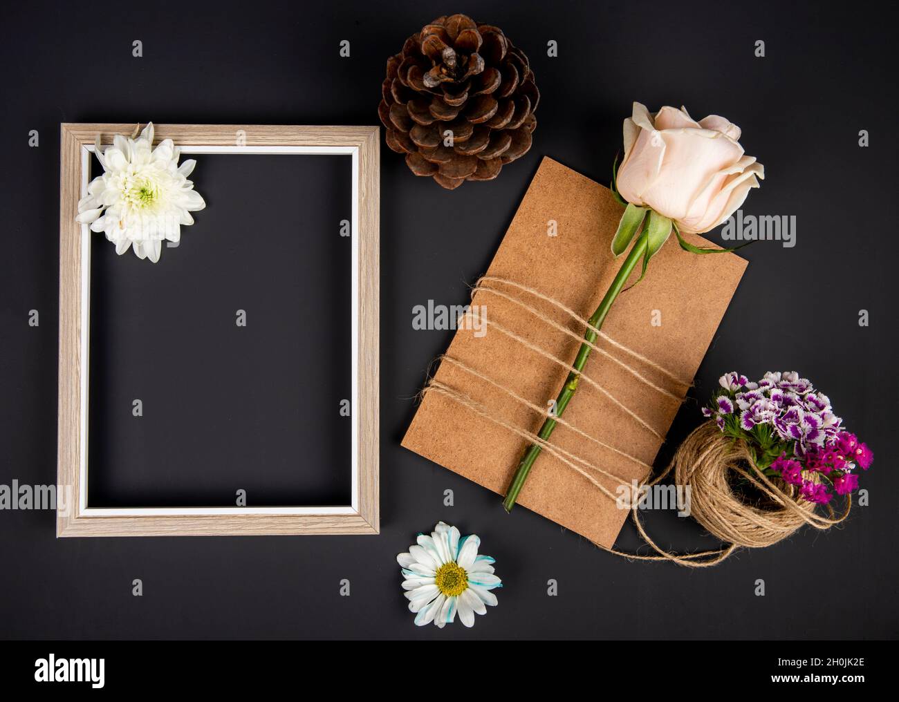 top view of an empty picture frame and brown paper greeting card with white color rose tied with a rope and turkish carnation with daisy flowers and c Stock Photo