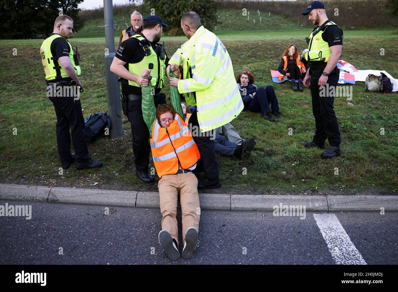 Police officers detain an Insulate Britain activist blocking a roundabout at a junction on the