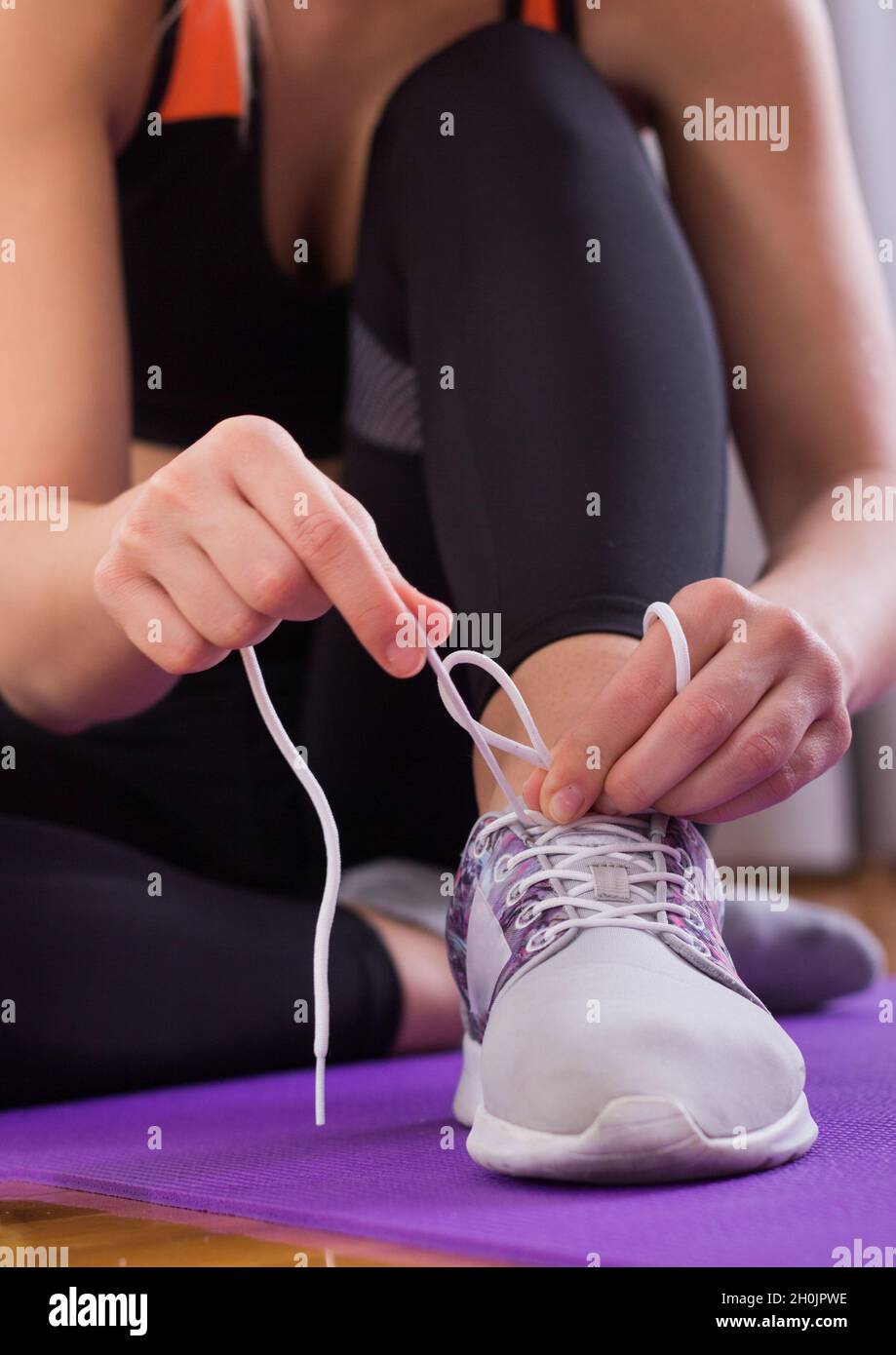 Image showcasing Attractive young woman sitting on yoga mat on parquet floor and tying ...