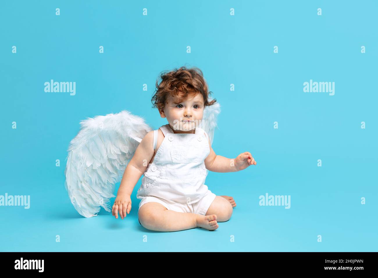 Portrait of cute toddler boy, baby in white romper with angel wings