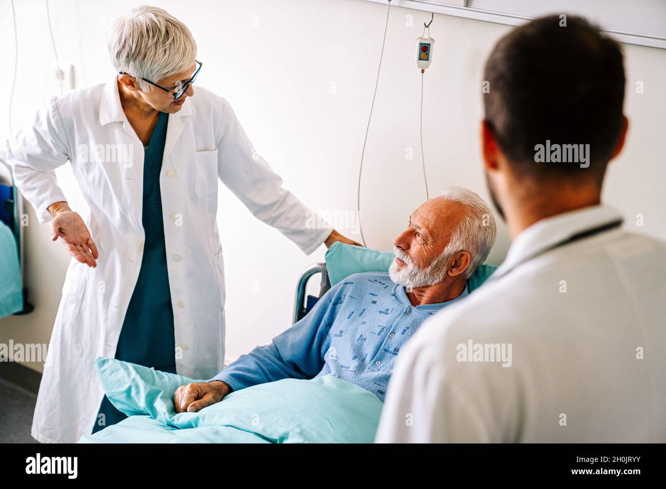 Doctor consulting happy senior man patient on hospital bed. Healthcare