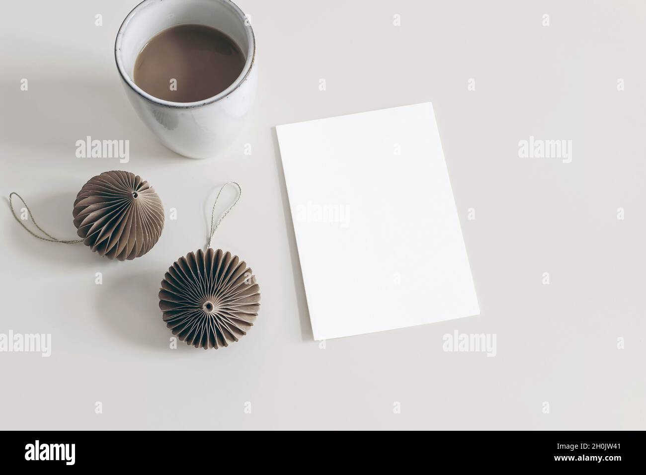 Winter holiday stationery mockup. Brown paper Christmas ornaments and cup of coffee isolated on white table background. Blank greeting card Stock Photo
