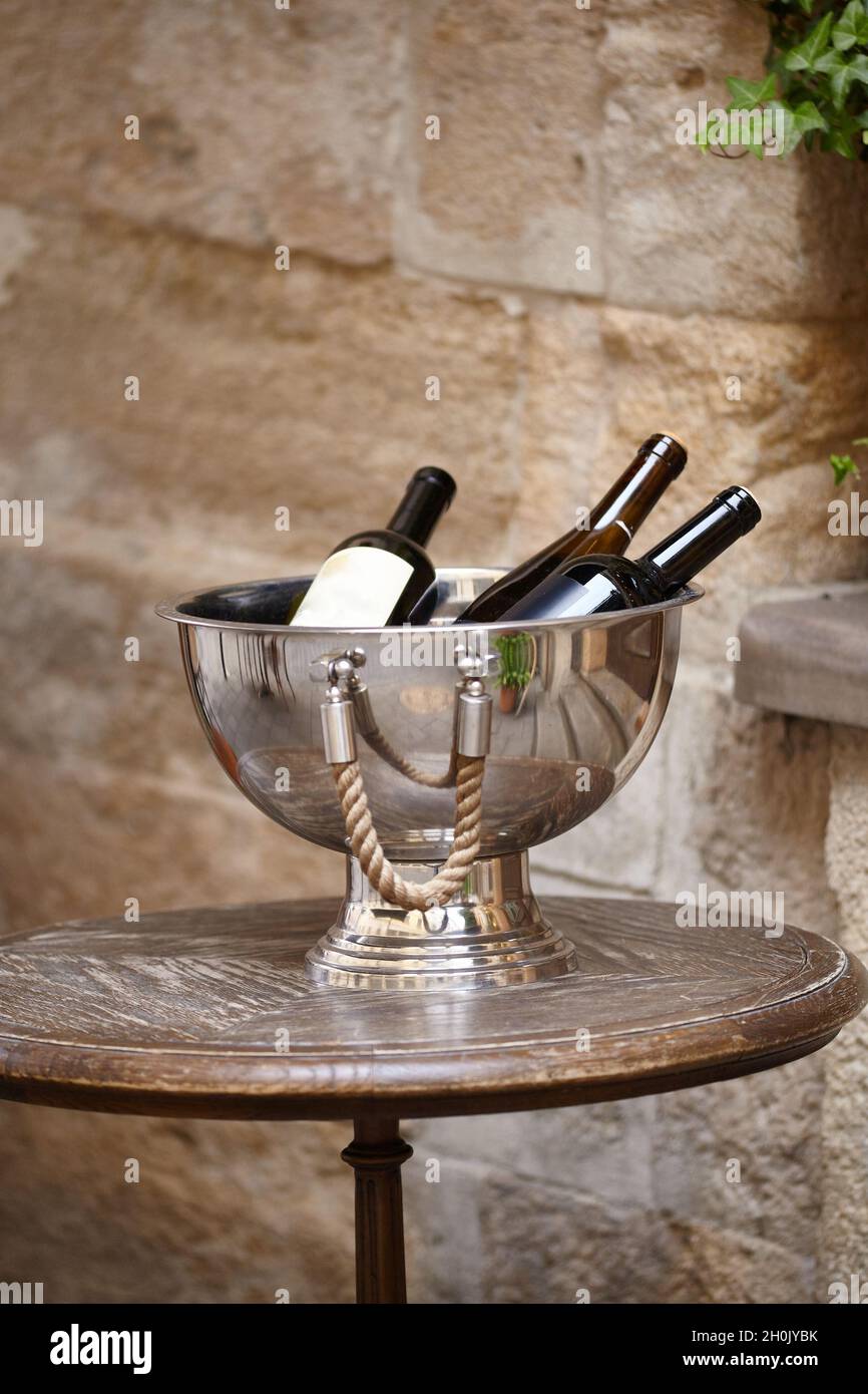 Wine bottles in a Large metal bowl standing on wooden table on the city street to attract visitors to the restaurant. Wine accessories Stock Photo