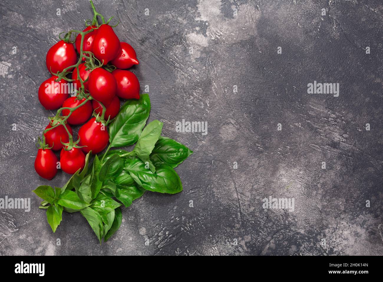 Cherry tomatoes and basil atop dark textured backdrop, copy space, top view Stock Photo