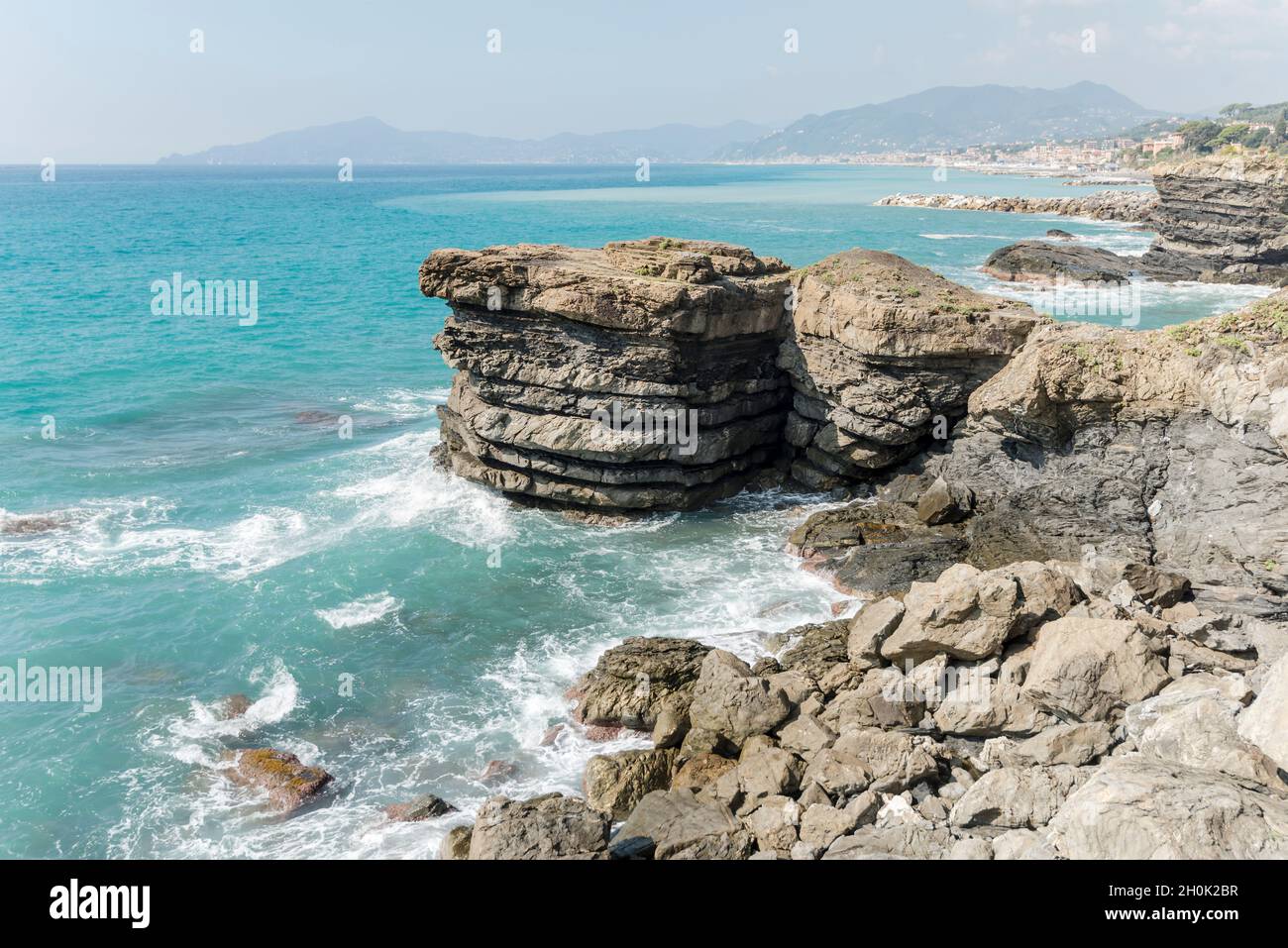 layered rocks of worn cliffs and Mediterranean sea waves at shore of Tigullio gulf, shot in bright fall light, Cavi, Genova, Liguria, Italy Stock Photo