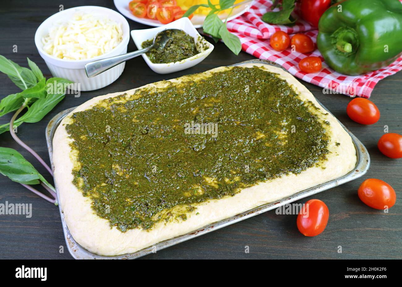 Homemade pizza dough with pesto sauce before baking in a messy kitchen Stock Photo