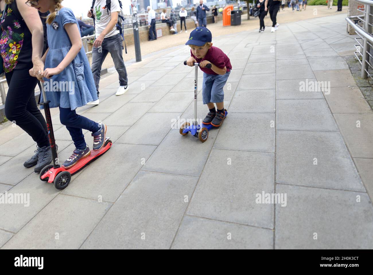 London, England, UK. Young boy on a scooter, with his mother and sister