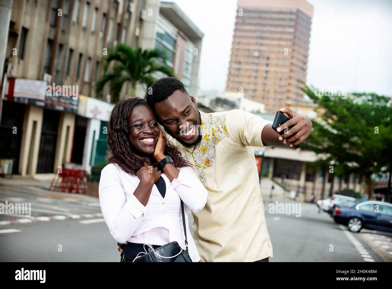 young couple standing outdoors photographing themselves smiling. Stock Photo