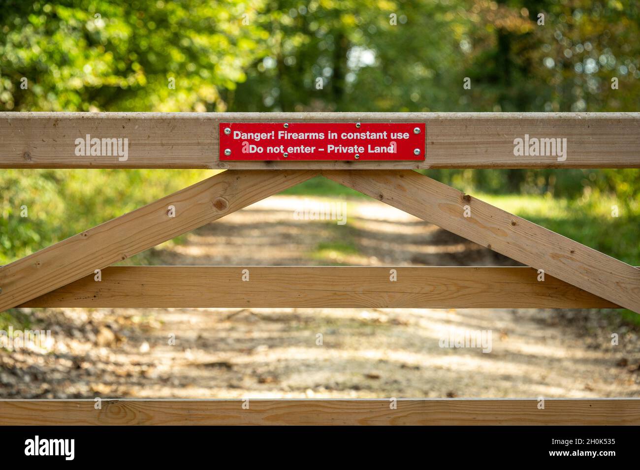 'Danger Firearms in constant use. Do not Enter, Private Land', sign on a wooden gate in the countryside. Stock Photo