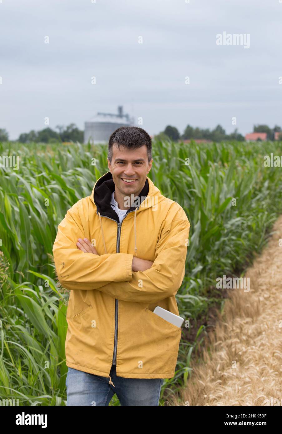 Smiling handsome farmer with crossed arms standing in front of corn ...