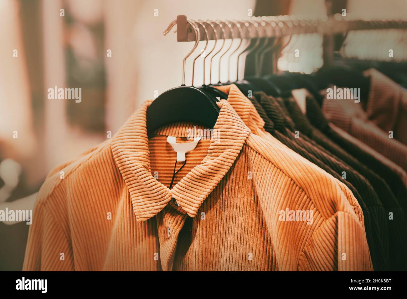 Beautiful corduroy coats for the autumn season in ginger and brown colors hang on hangers in a clothing store in the mall. Shopping. Stock Photo