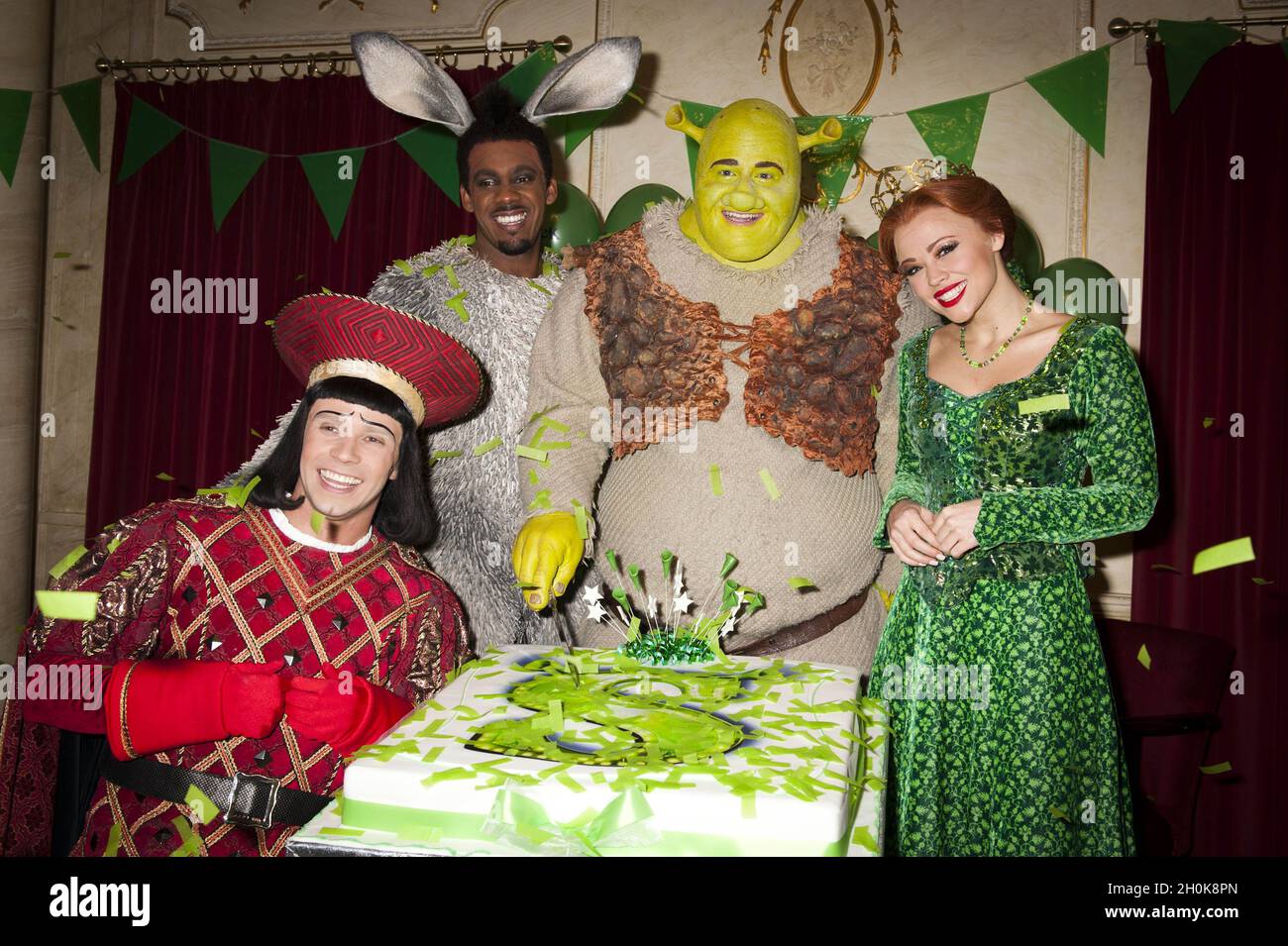 Neil McDermott who plays Lord Farquaad, Richard Blackwood who plays Donkey, Dean Chisnell who plays Shrek and Kimberley Walsh who plays Princess Fiona cut the cake at Shrek The Musical 1 Year Anniversary Family Fete at the Drury Lane Theatre in London Stock Photo