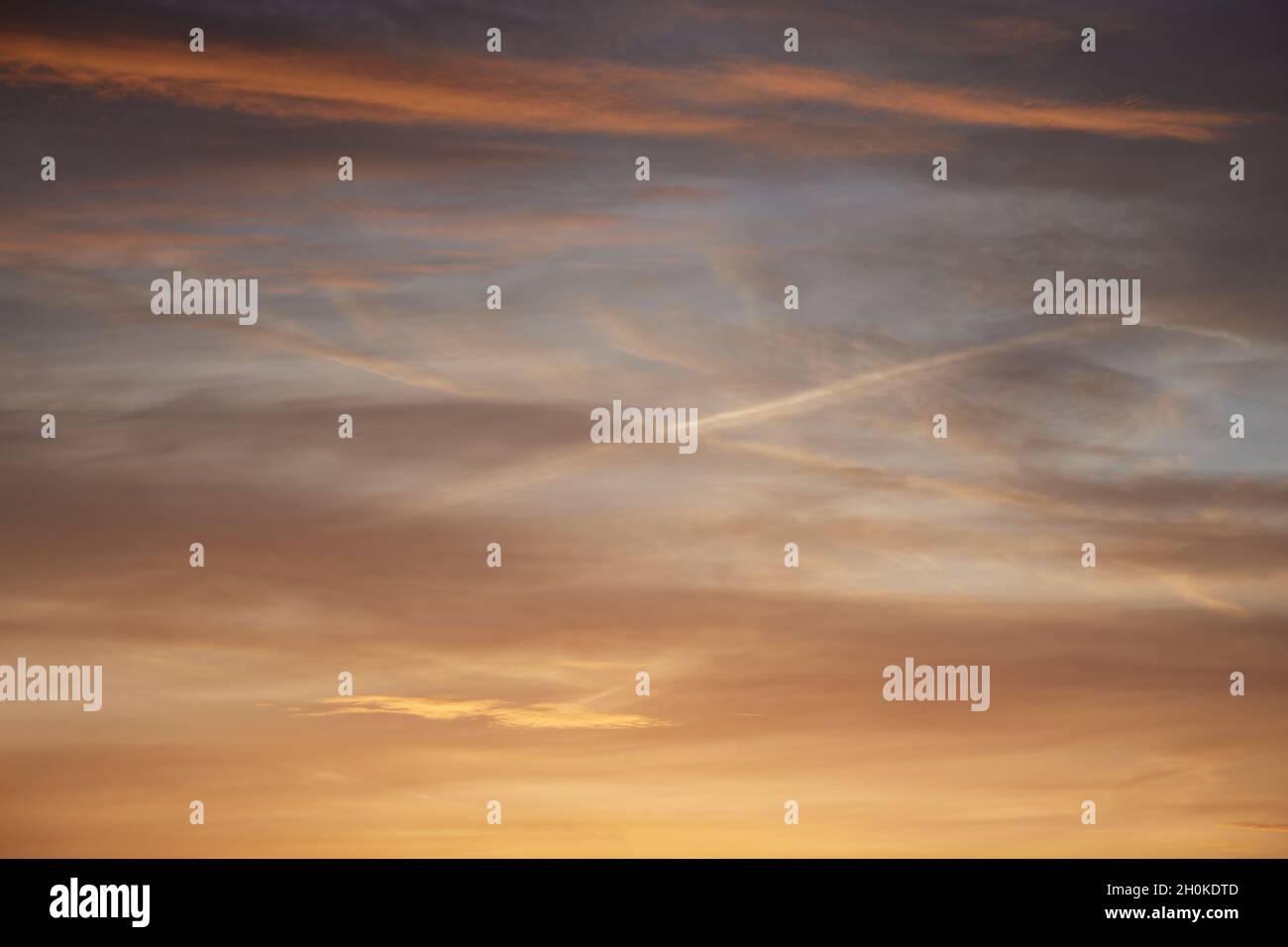 Contrails can be seen creating a cross with diagonal lines in the colourful early morning sky. Stock Photo
