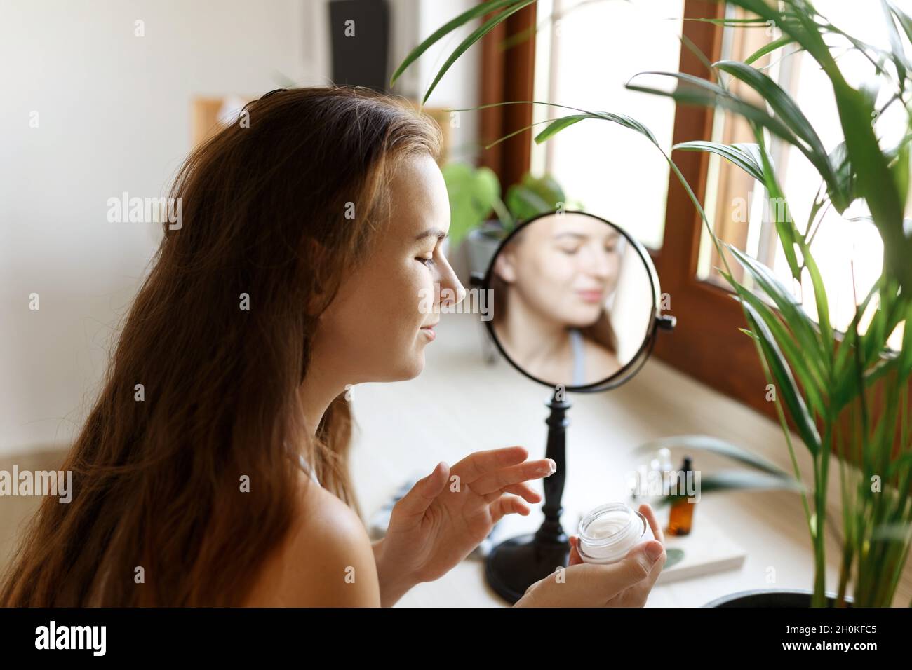 Beauty girl looking at mirror while touching her face and applying ...