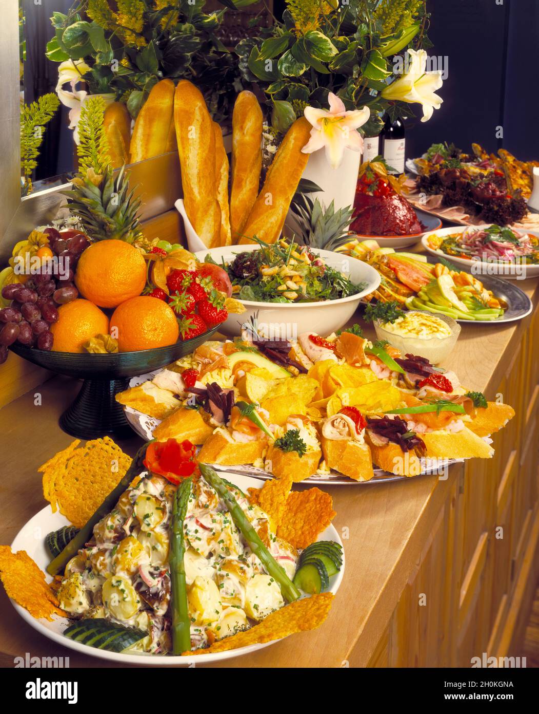 Portrait format, buffet dishes  with mirror , flowers, baguettes, french bread, potato salad, smoked salmon, chicken dishes on light wood table Stock Photo