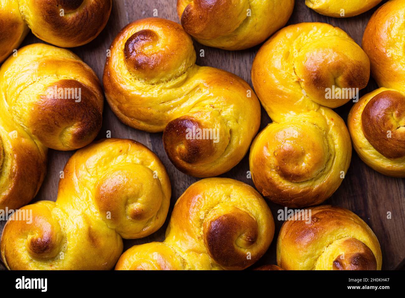 A background of Swedish traditional christmas bun Lussekatter or Lussebullar on a rustic wooden table. The buns are freshly made and homemade and the Stock Photo