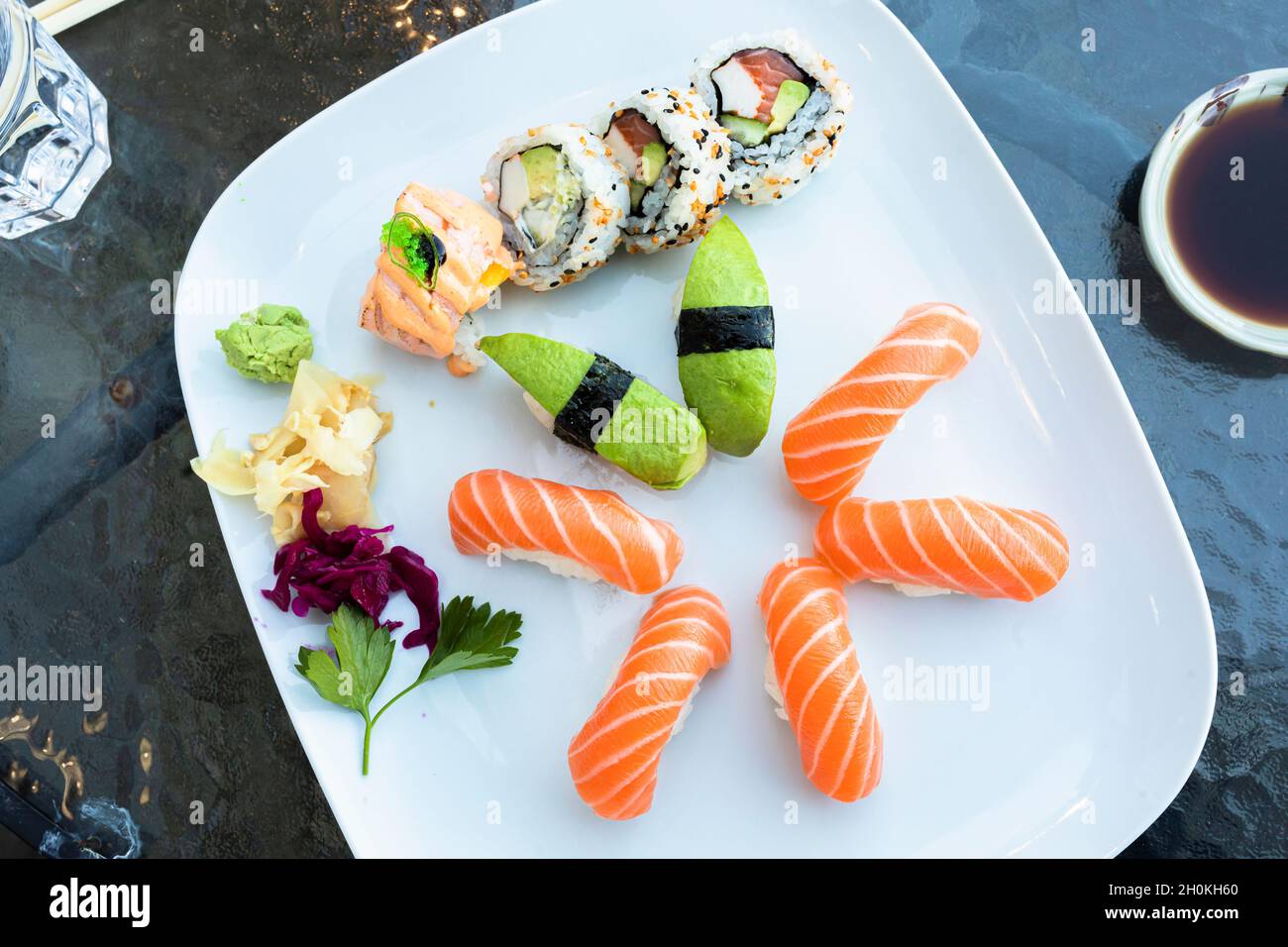 Sushi plate on a table outdoors at a restaurant. The plate has nigiri sushi with salmon, nigiri sushi with avocado and california rolls. Healthy diet Stock Photo