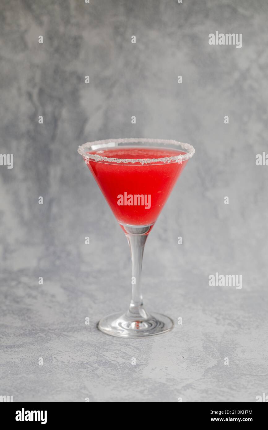 A red drink in a martini glass with a sugar or salt coated  edge. With a gray background. Stock Photo