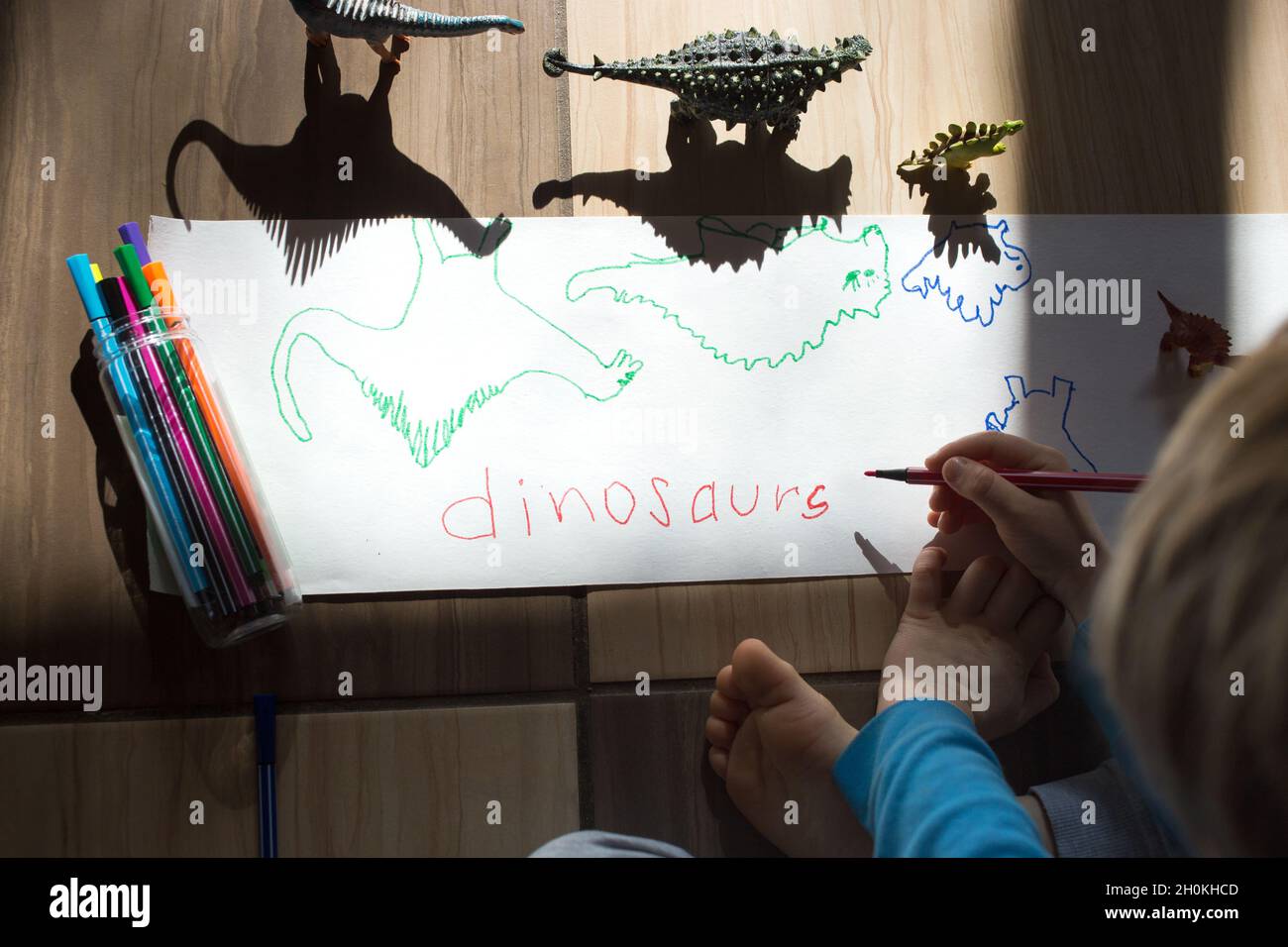 child sits on the floor and draws the contrasting shadows of the dinosaur action figures with a felt-tip pen. ideas for children's creativity. Games w Stock Photo