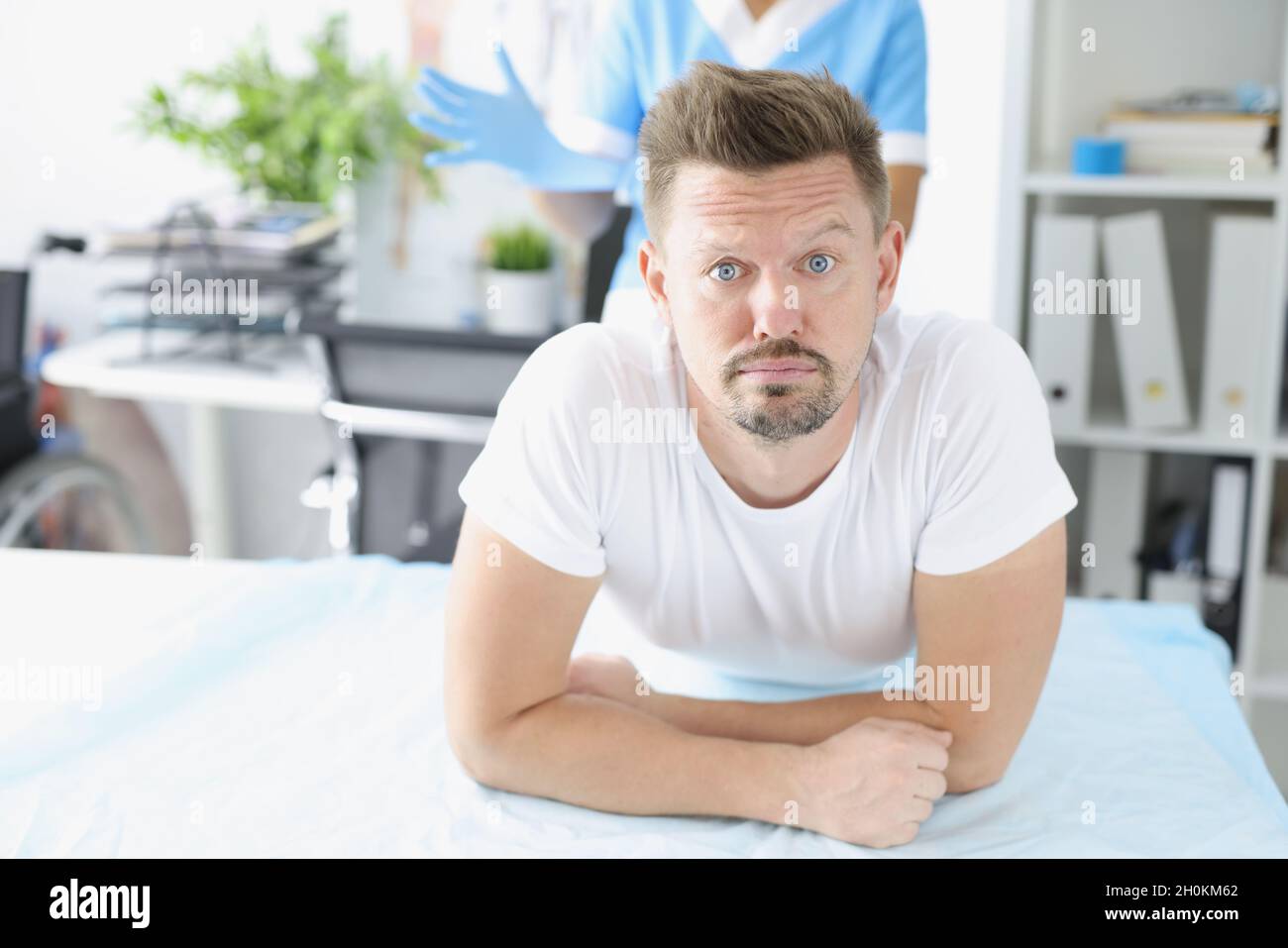 Young sad man lying on couch in front of doctor proctologist in clinic Stock Photo