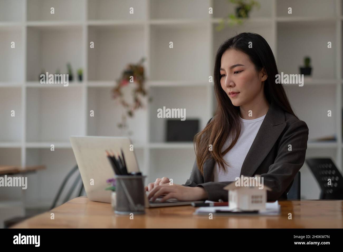 Real estate agent hand typing laptop keyboard with house model and keys