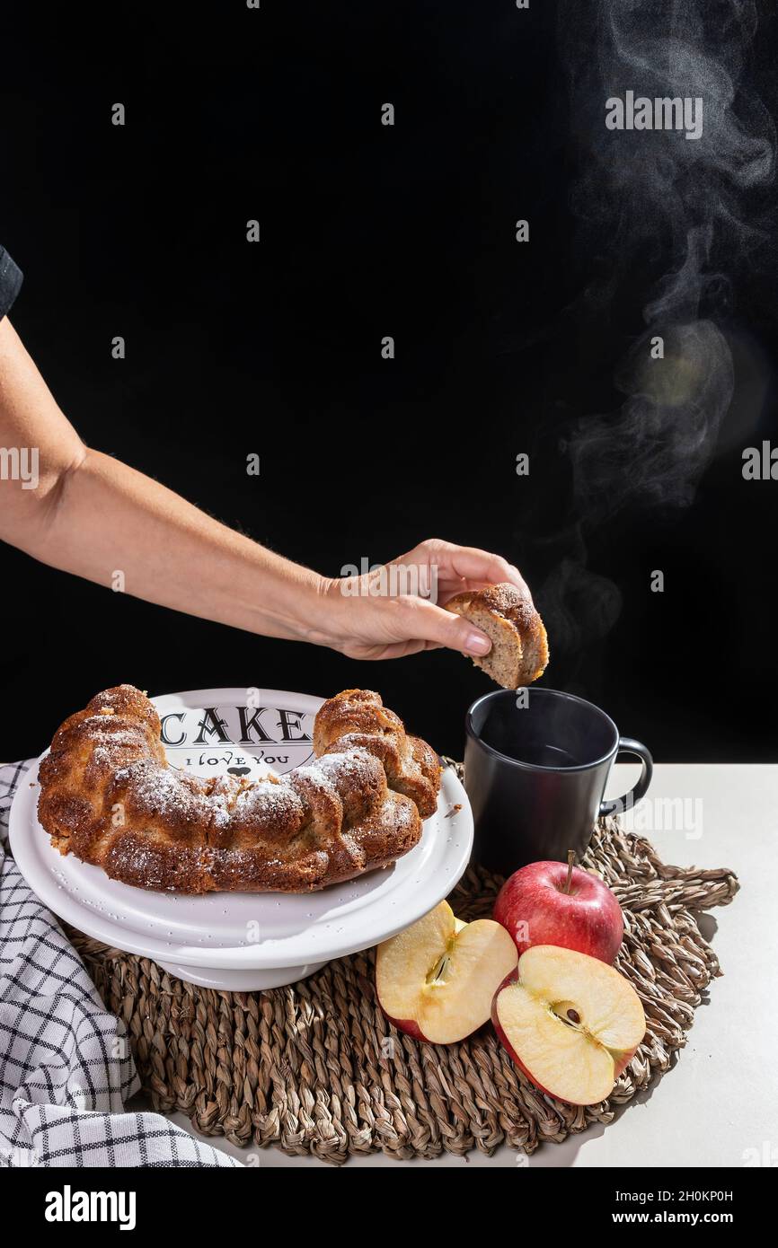 A female hand is about to dip a slice of donut into a smoking hot drink Stock Photo