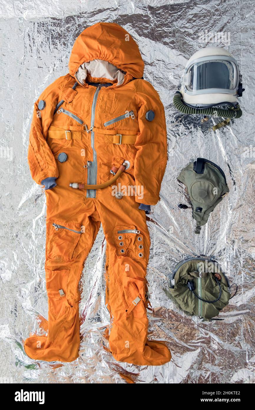 Flat lay of astronaut orange space suit, space helmet and space suit accessories on silver