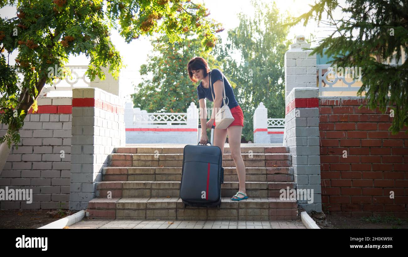 woman with a heavy suitcase hardly climbs the stairs of the railway
