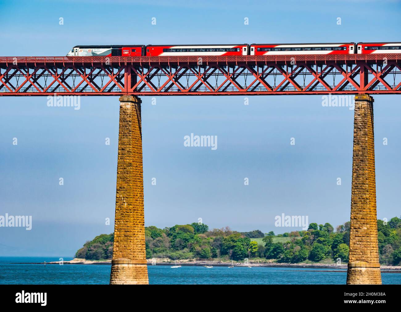 LNER train crossing iconic Forth Rail Bridge over Firth of Forth on sunny day, Scotland, UK Stock Photo