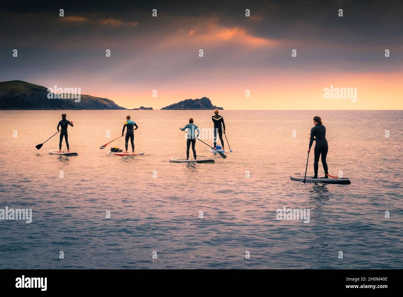 A group of Stand Up Paddleboarders paddling across Fistral Bay in evening light at Newquay in Cornwall. Stock Photo