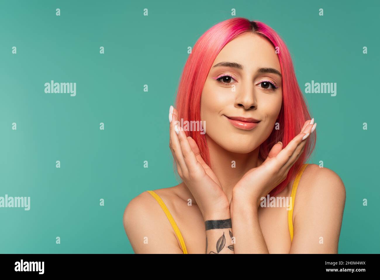 tattooed young woman with pink dyed hair smiling isolated on turquoise Stock Photo