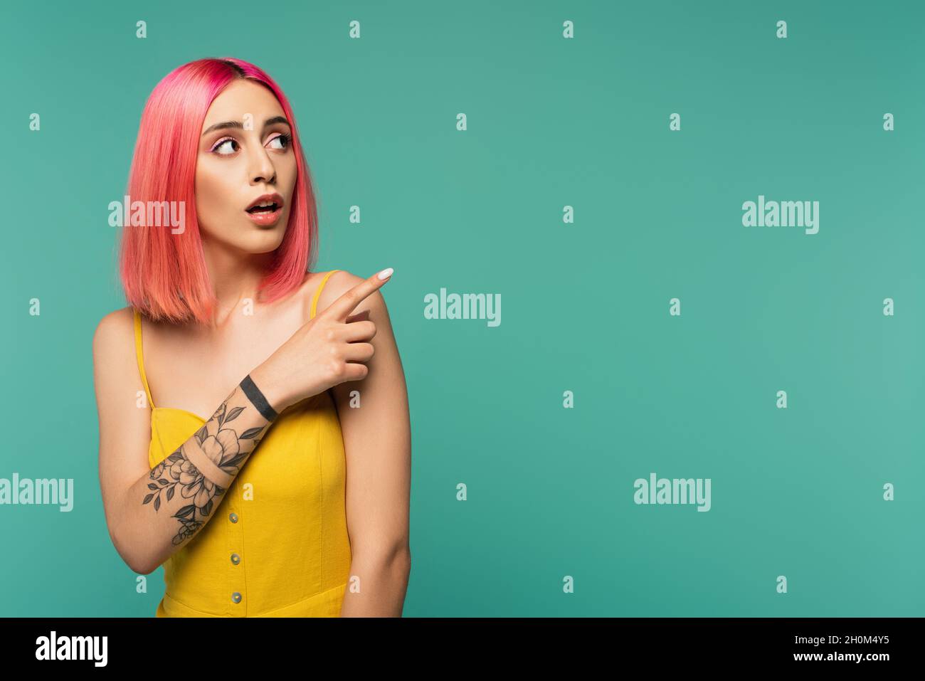 amazed young woman with pink dyed hair poising with finger isolated on turquoise Stock Photo