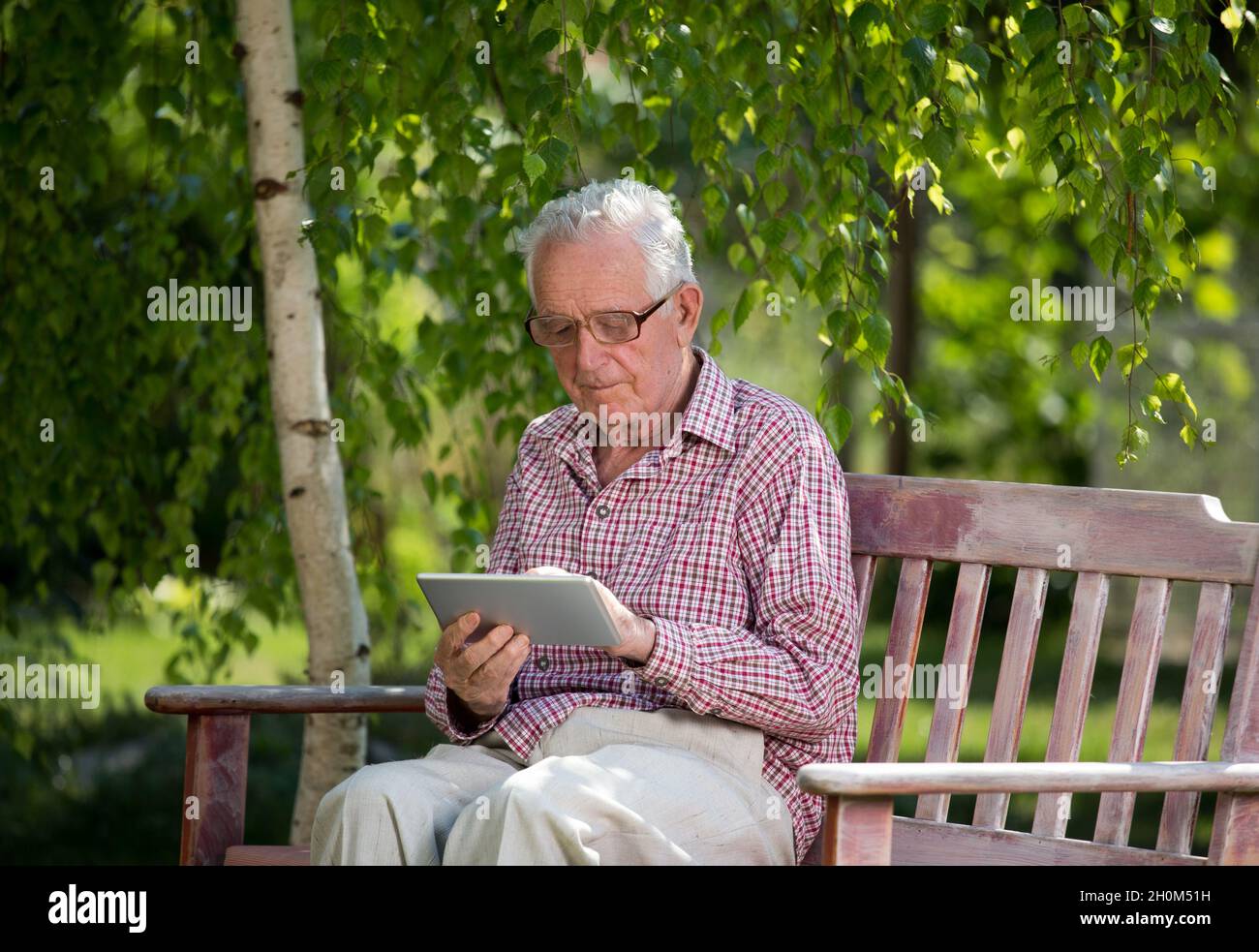 Old man sitting on bench in park and looking at tablet Stock Photo - Alamy