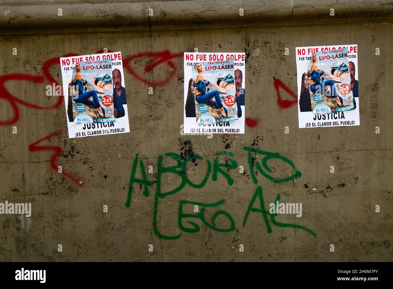 Feminist graffiti on base of monument demanding the right to legal abortion for women. Above it are posters offering 2 for 1 laser liposuction surgery pasted over left wing posters demanding justice for a supposed coup after the controversial presidential elections of 20th October 2019. Av 16 de Julio / El Prado, La Paz, Bolivia Stock Photo