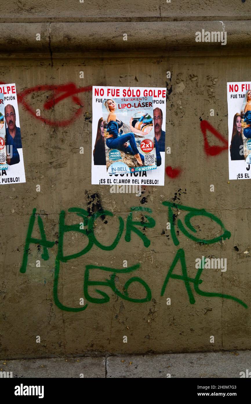 Feminist graffiti on base of monument demanding the right to legal abortion for women. Above it are posters offering 2 for 1 laser liposuction surgery pasted over left wing posters demanding justice for a supposed coup after the controversial presidential elections of 20th October 2019. Av 16 de Julio / El Prado, La Paz, Bolivia Stock Photo