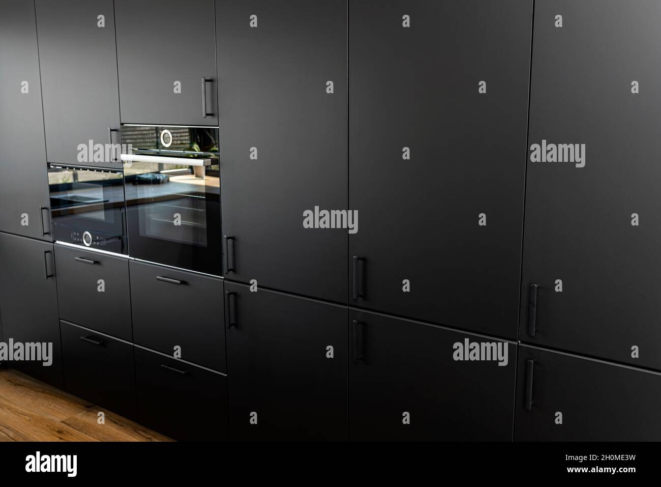Modern kitchen with black fronts, built in oven and microwave, vinyl panels on the floor. Stock Photo