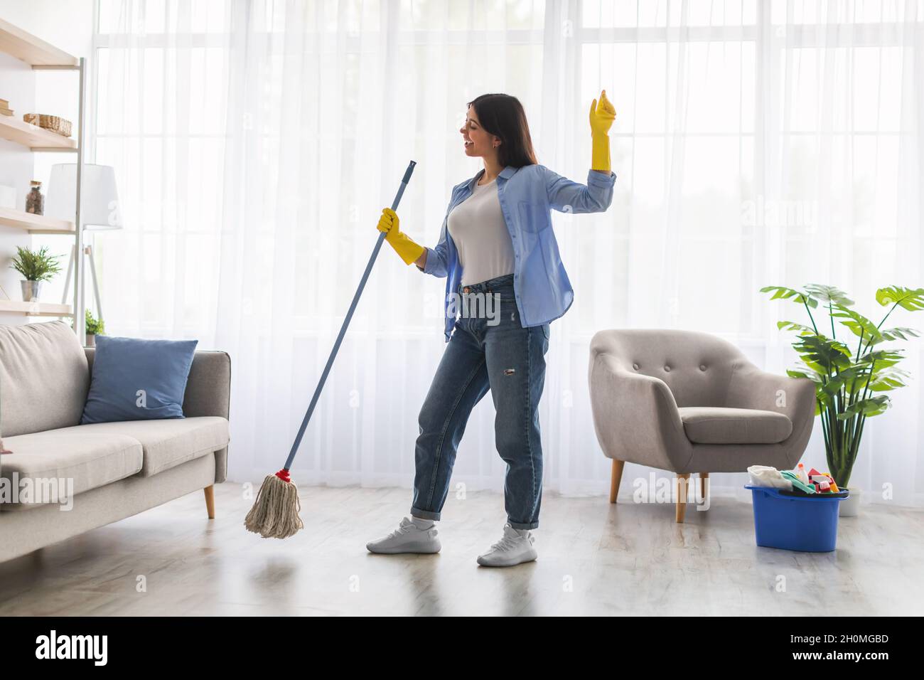 Excited woman cleaning floor singing, dancing and holding mop Stock