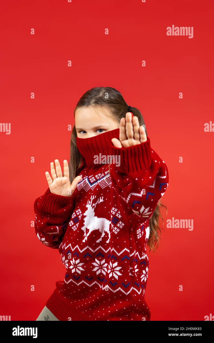 portrait of cheerful girl in red Christmas sweater with reindeer and with collar on half face showing ninja isolated on red background Stock Photo