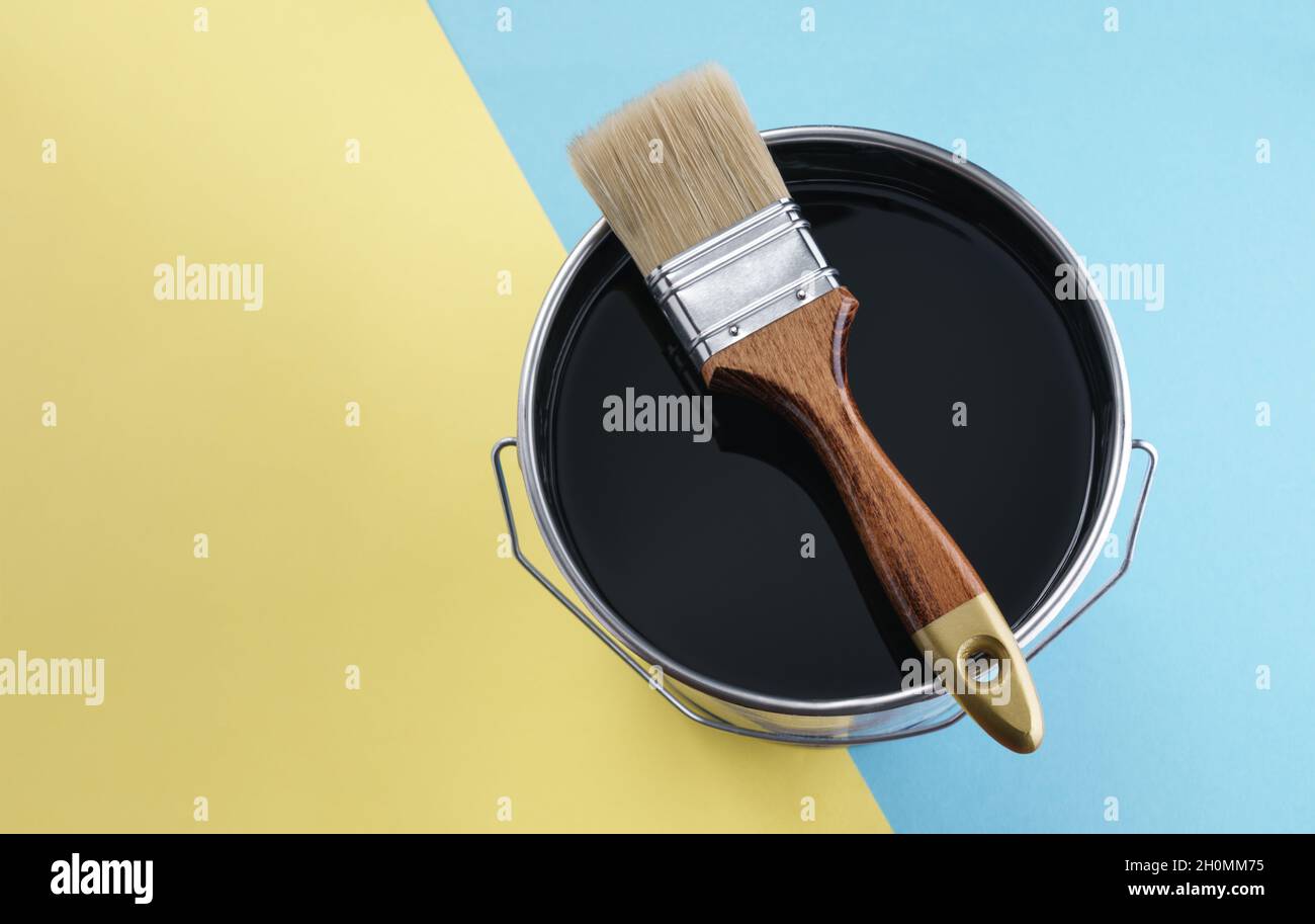 Wooden brush on black color paint can on blue and yellow background Stock Photo