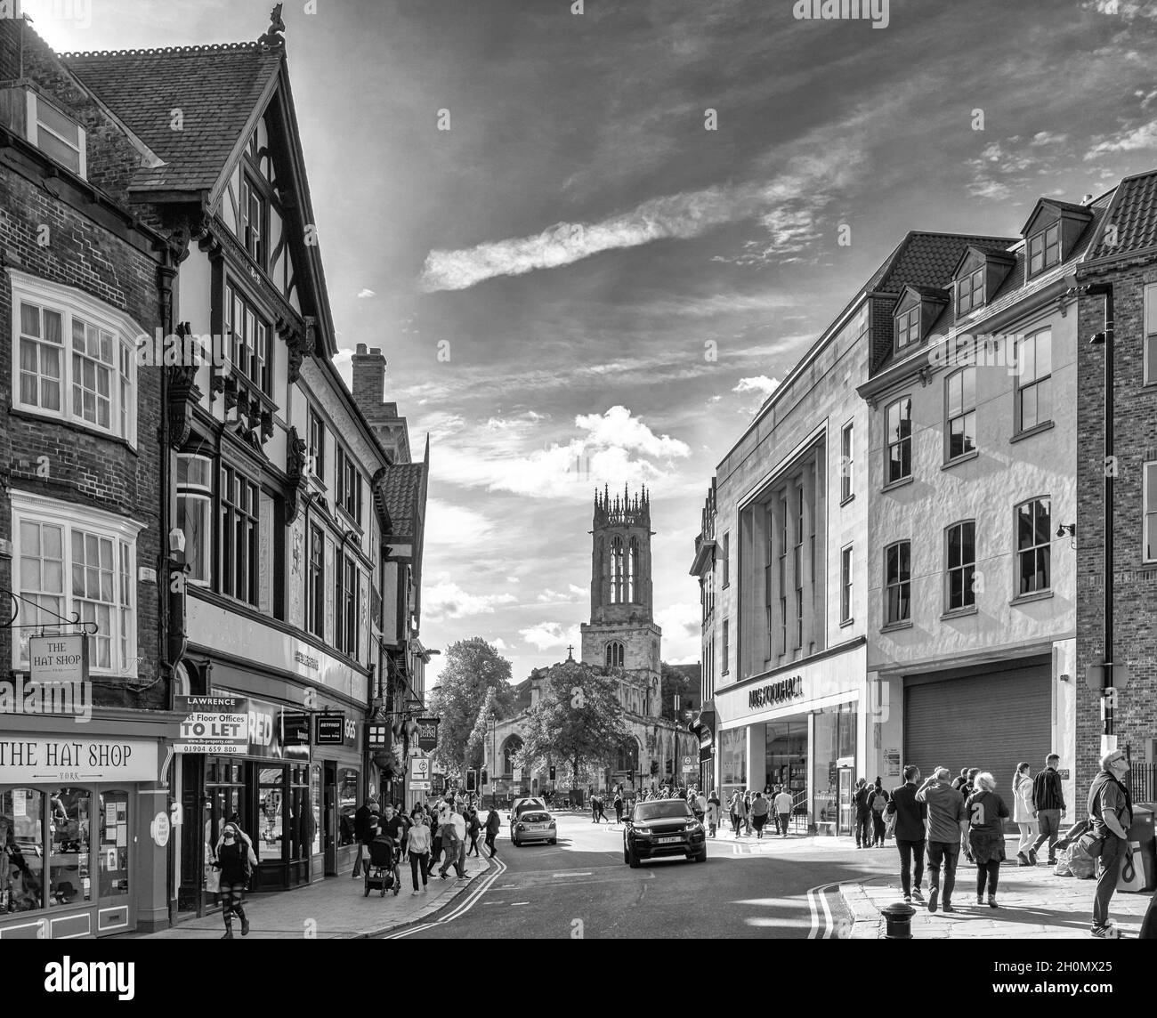 City street leading to a church.  Shops are on either side and people are in the street.  A sky with light clouds is above. Stock Photo