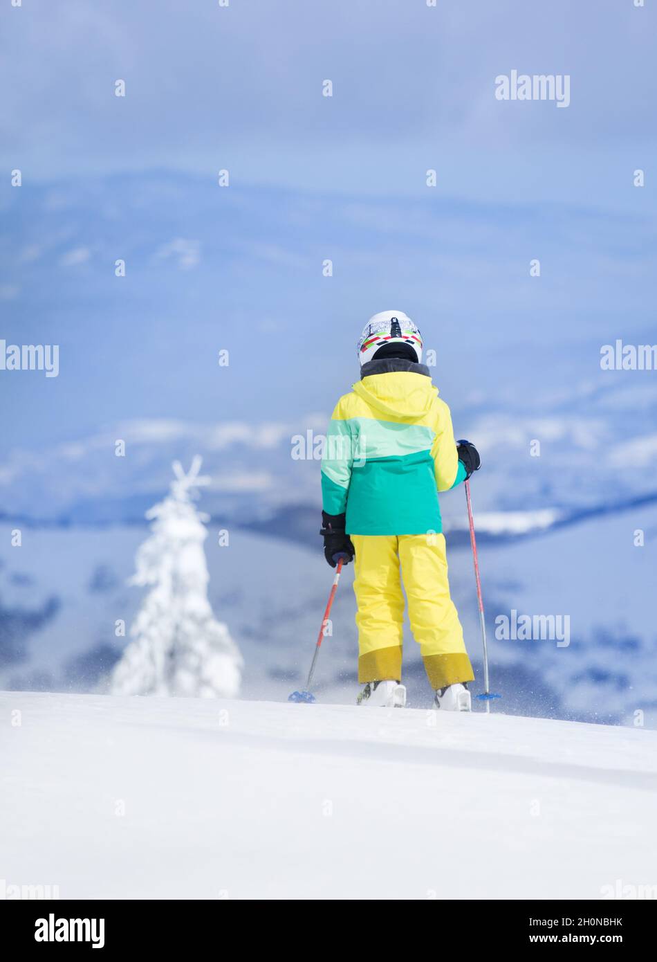 Rear view of child skiing on peak of mountain. Winter sport and recreation concept Stock Photo