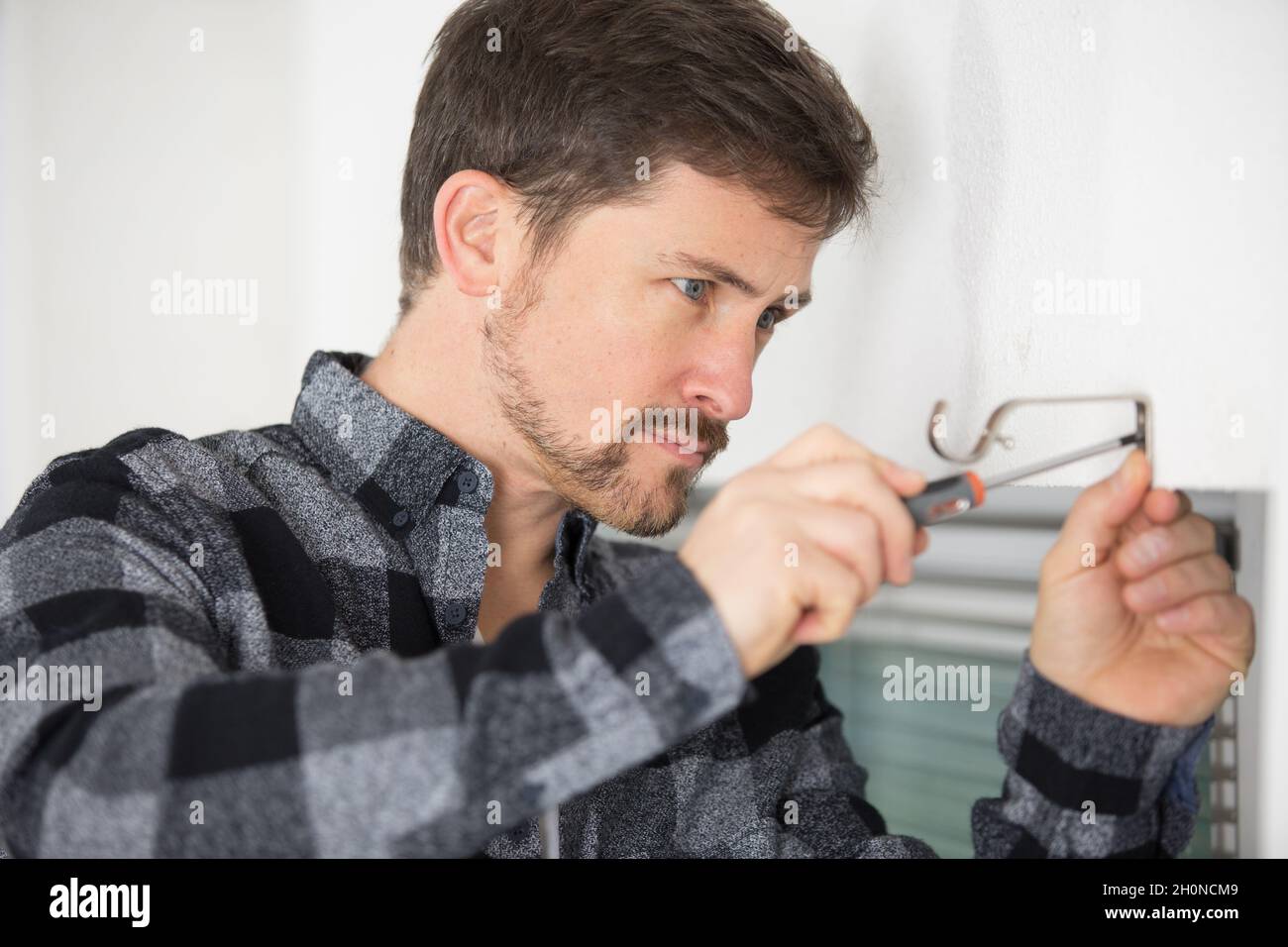 handyman installing window curtain rod support on the wall Stock Photo