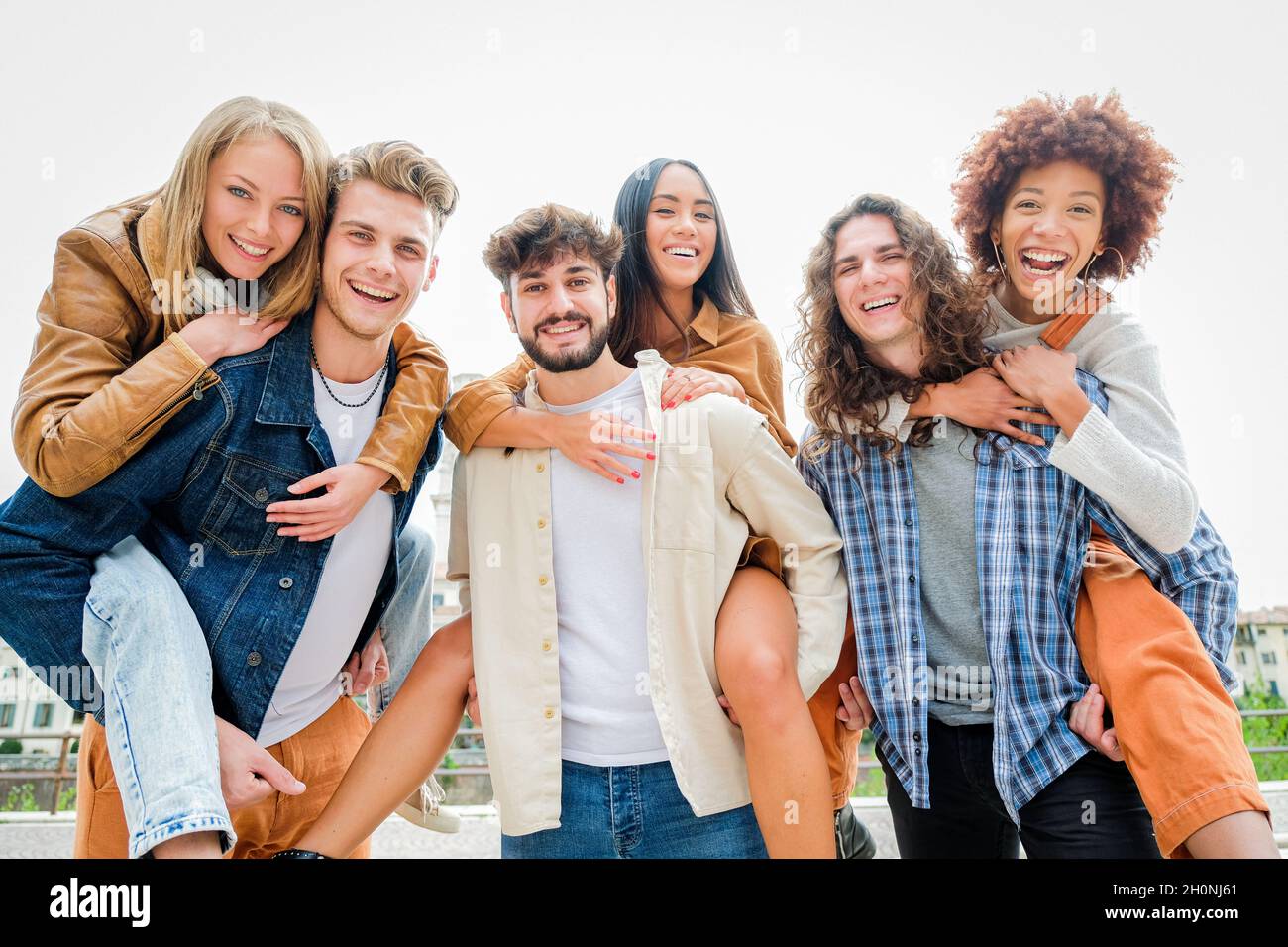 Young Friends having Fun Outdoors - Six students outdoors, men carrying two girls on their backs Stock Photo