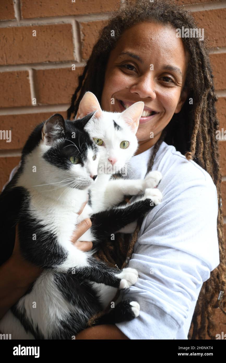 Woman smiles while holding two cats Stock Photo
